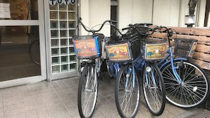 Drei Fahrräder mit Körben, vor einem Gebäude, an dem ein Schild mit der Aufschrift 'TOYO' hängt.