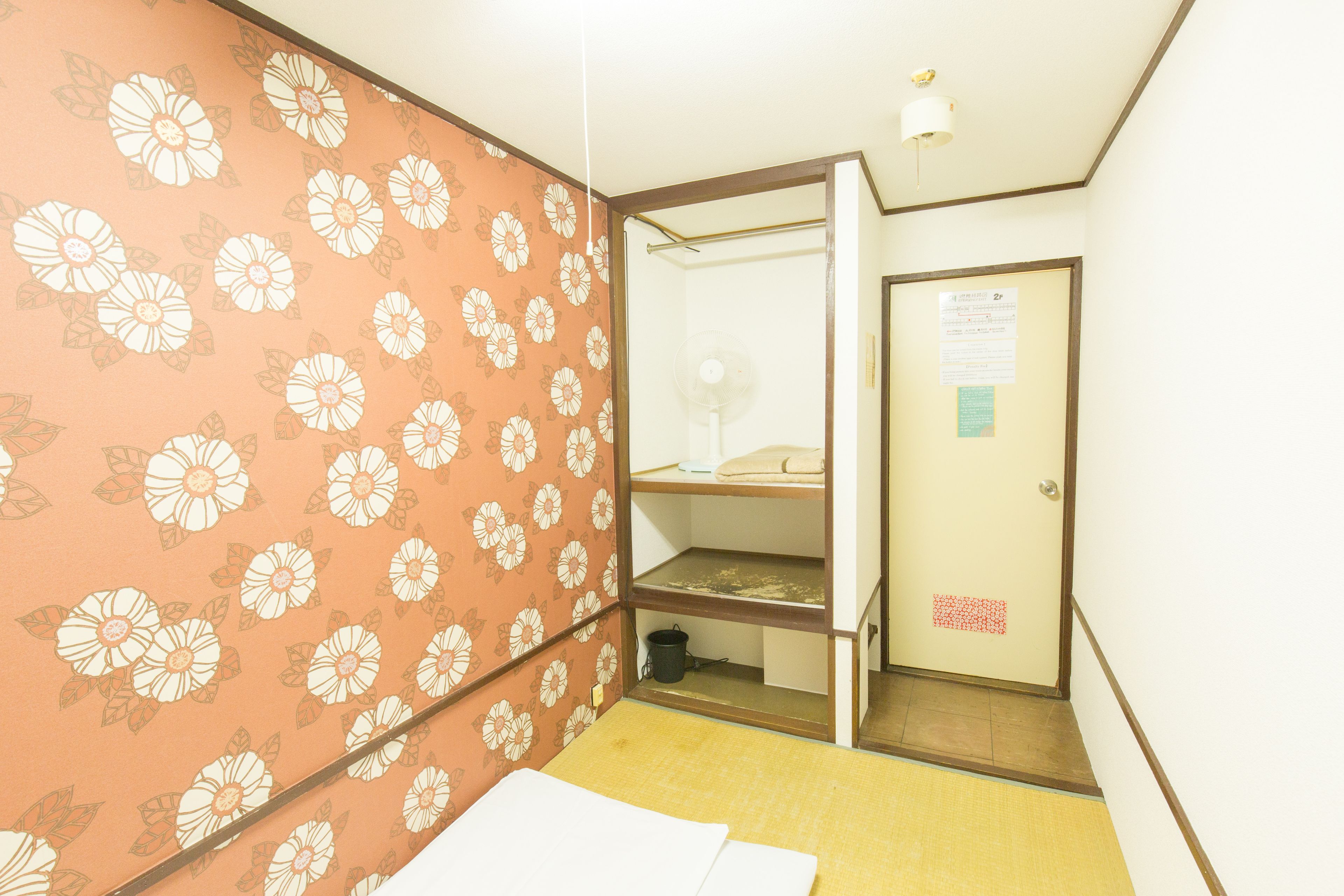 A room with a floral wallpaper, a wooden shelf unit, and a door with a notice.