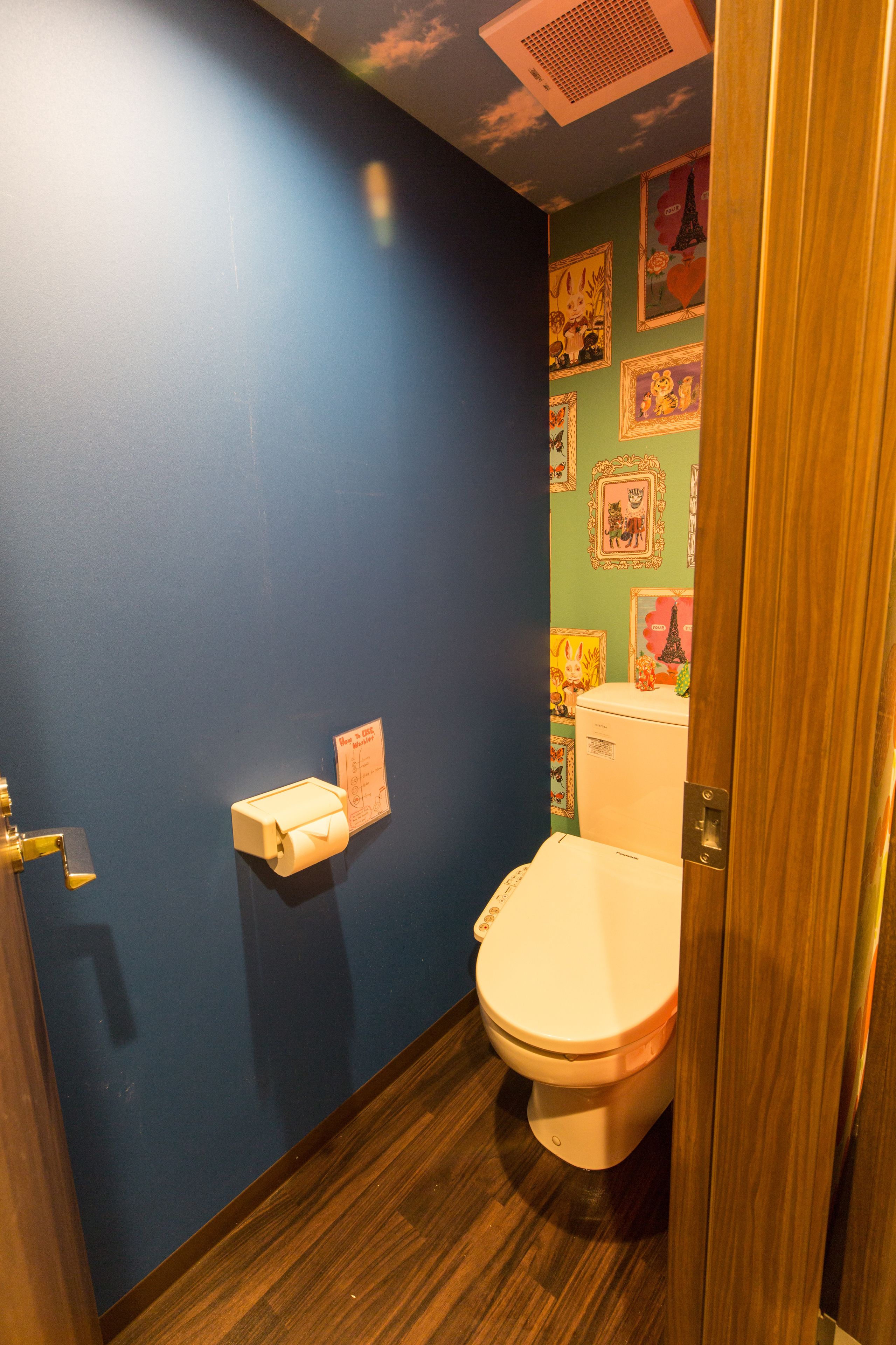 Un baño pequeño con pared azul, suelo de madera y un inodoro con tapa blanca.