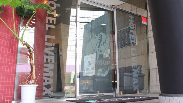 A hotel entrance with large glass doors, a potted plant, and a sign indicating the hotel's name. - HOTEL LiVEMAX Fuchu Annex (Fuchu)