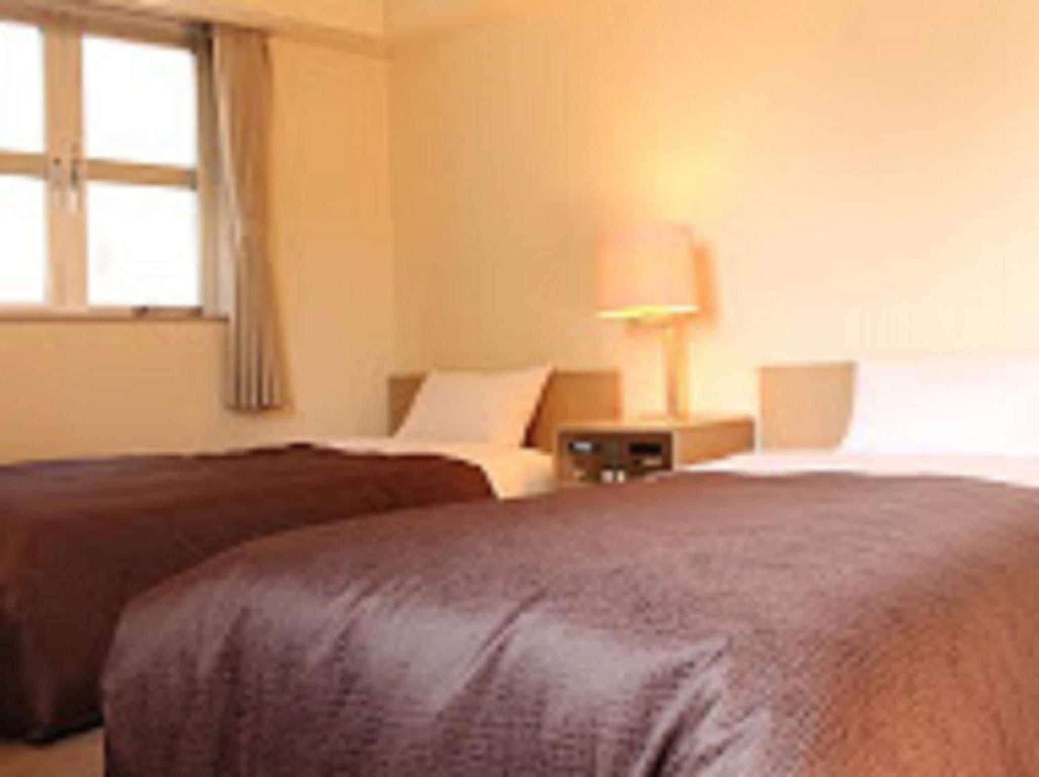 A hotel room with two beds, a nightstand, a lamp, and a window with curtains.