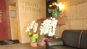 A hotel reception area with a clock, a reception desk, and two potted orchids. - HOTEL LiVEMAX Fuchu Annex (Fuchu)