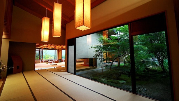 Un intérieur japonais traditionnel avec un sol recouvert de tatamis, des portes coulissantes et une vue sur un jardin, visible à travers de grandes fenêtres.
