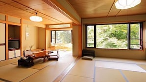 Une pièce de style japonais traditionnel, avec un sol recouvert de tatamis, une table basse, un canapé et une grande fenêtre donnant sur un paysage verdoyant.