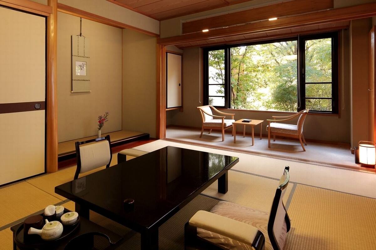 A traditional Japanese-style room with tatami flooring, a low table, and a view of greenery through large windows.