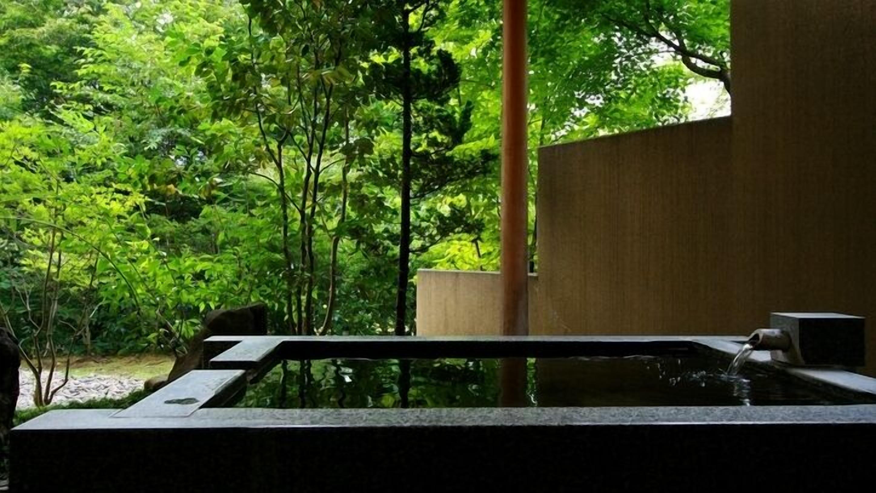 Een jacuzzi in een weelderige tuin met een houten constructie en een stenen muur.