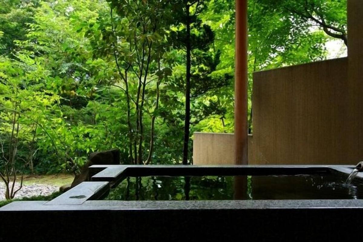 A hot tub in a lush garden with a wooden structure and a stone wall.