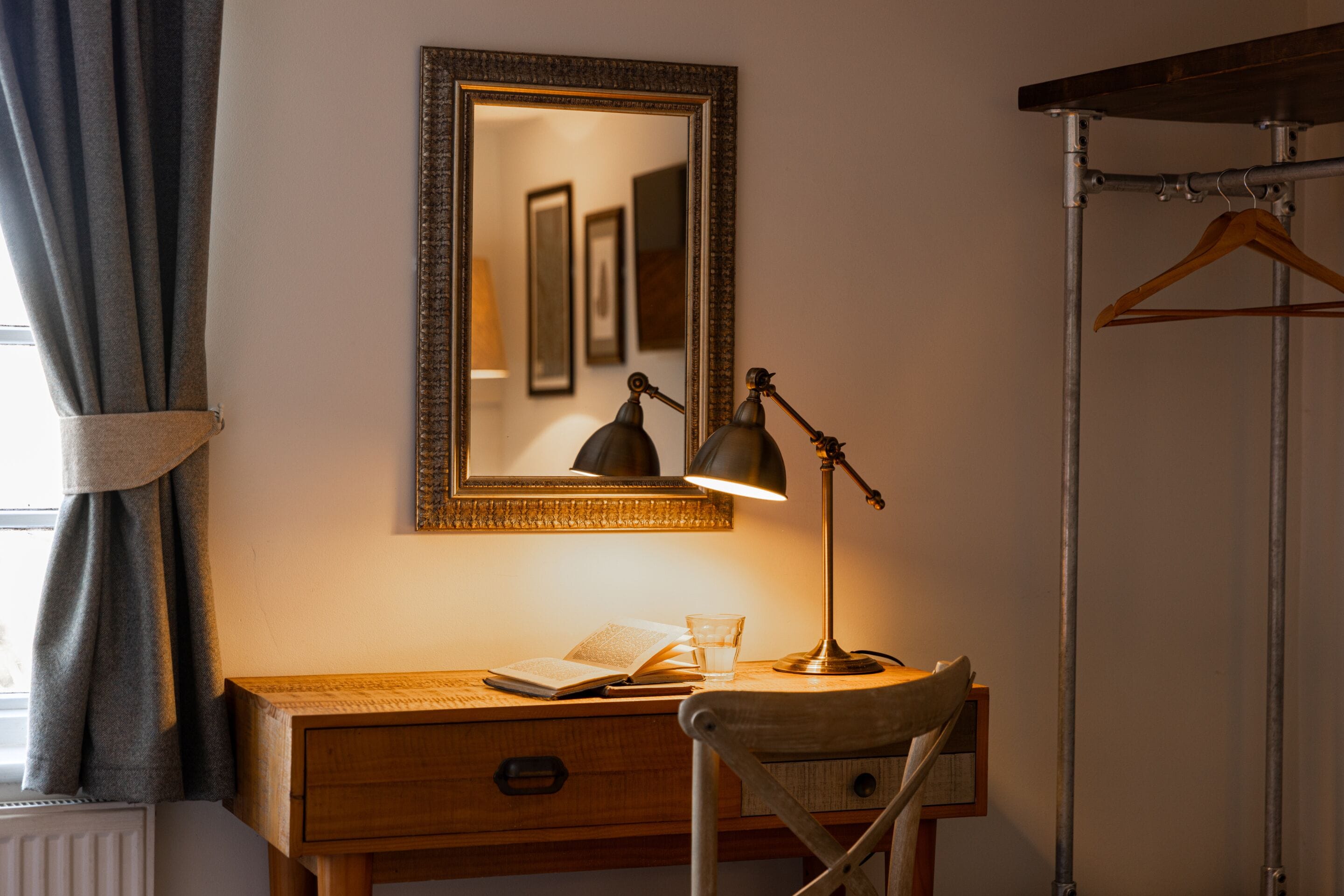A wooden desk with a lamp, a mirror, and a chair.