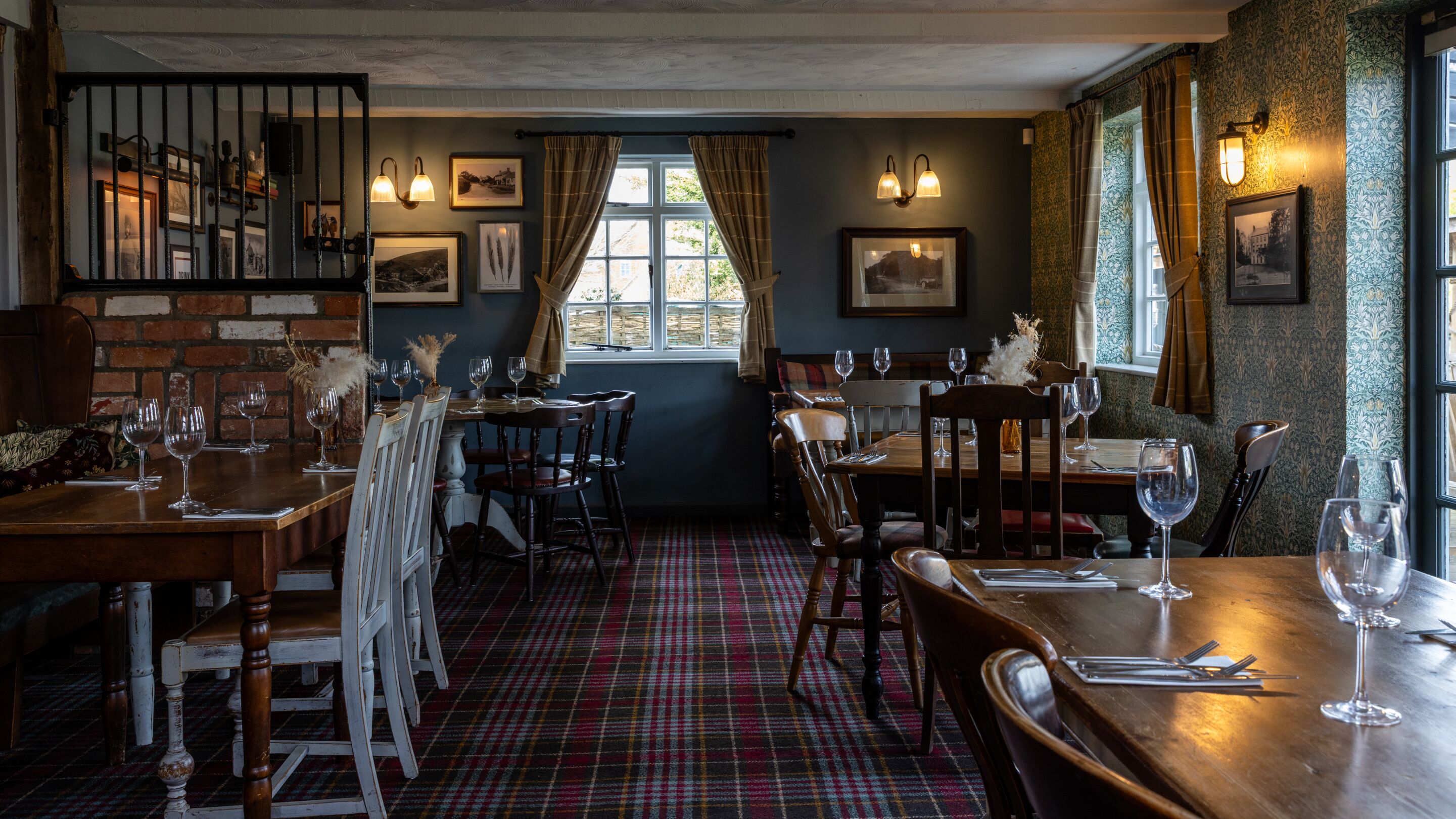 A restaurant with wooden tables and chairs, plaid carpeting, and framed pictures on the walls.