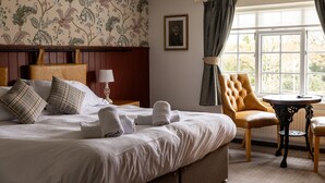 A hotel room with a bed, a chair, a table, and a window with curtains. - The Countryman Inn (Dorchester)