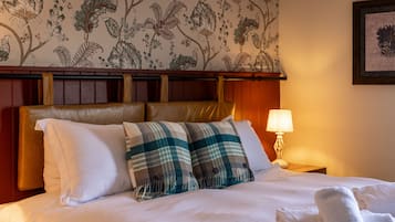 Una cama bien hecha con sábanas blancas, dos almohadones a cuadros y un cabecero con diseño de papel tapiz floral.