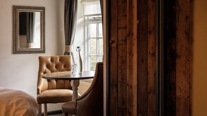 A room with a bed, a wooden chair, a small table with a candle and a glass, and a window with curtains. - The Countryman Inn (Dorchester)