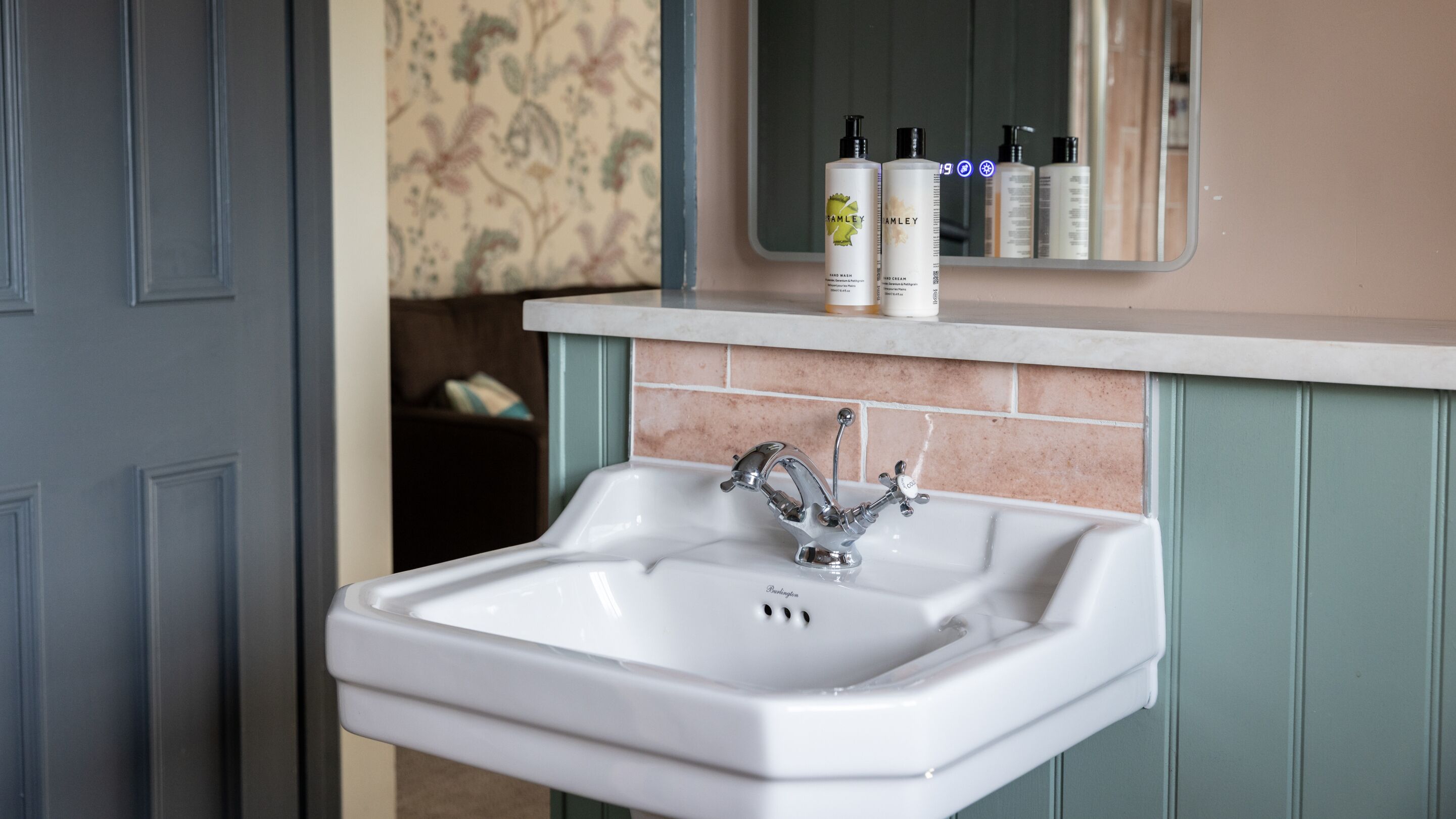 A bathroom with a white sink, a mirror, and toiletries on the countertop.