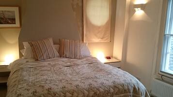 A bedroom with a floral bedspread, two striped pillows, a nightstand with a lamp, and a window with a view.