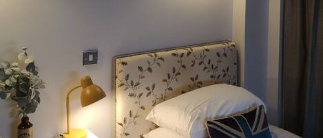A bedroom with a bed, a nightstand, a lamp, a wall-mounted light, and a decorative fish wall art piece.