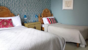 A room with two beds, a nightstand with a lamp, and a wall with a patterned wallpaper and a framed picture.