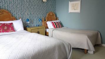 A room with two beds, each with a wooden headboard, a nightstand with a lamp, and a wall with a patterned wallpaper and a framed picture.