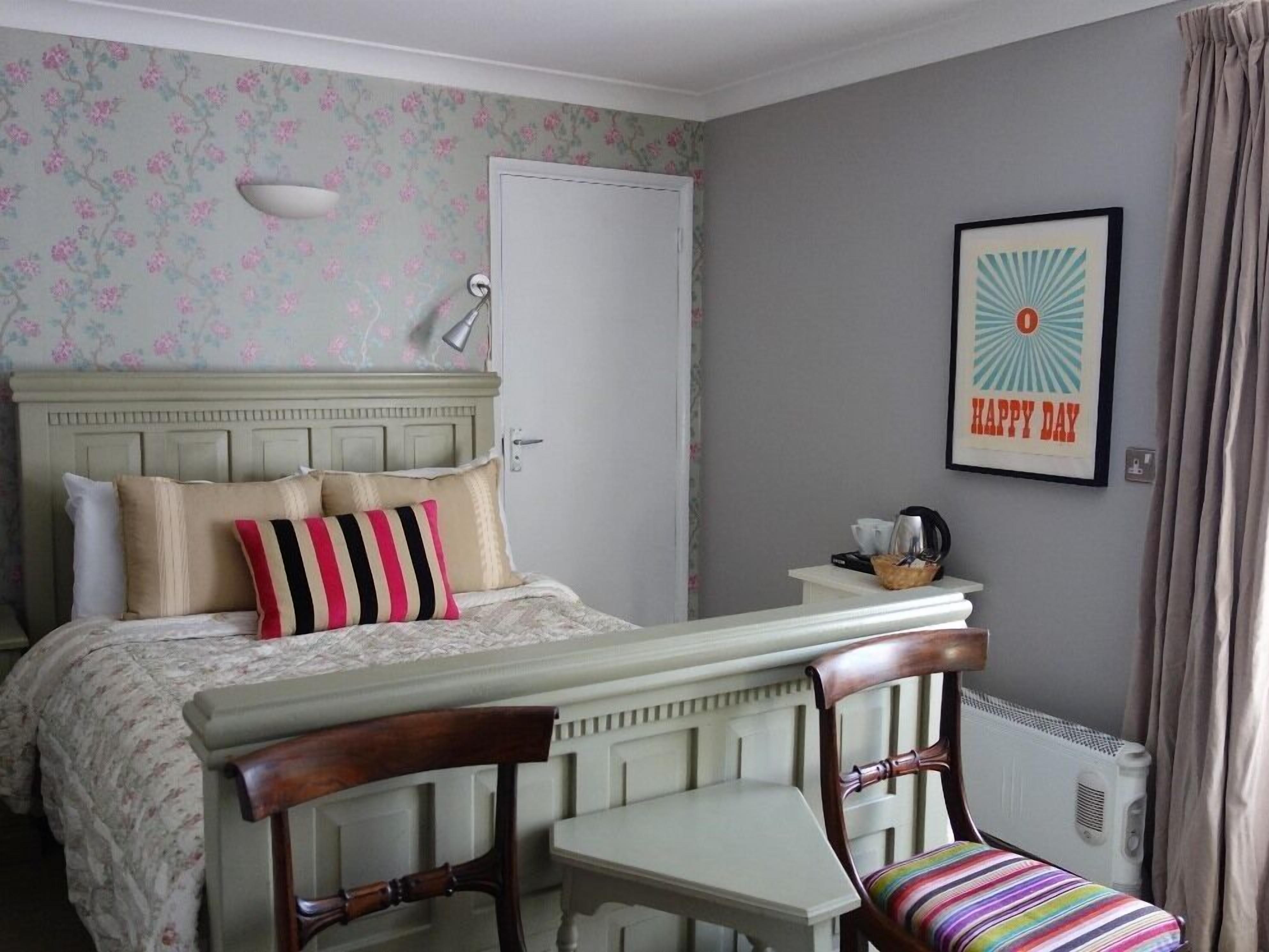 Ein Schlafzimmer mit einem Bett, zwei Sesseln, einem kleinen Tisch, einer Heizung und einem gerahmten Bild an der Wand.