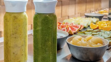 Two bottles of green and yellow beverages, a bowl of sliced fruits, and a bowl of peeled potatoes.