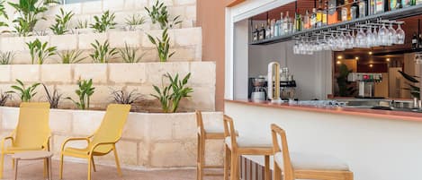 A bar area with a stone wall, wooden chairs, and a bar counter with various bottles and glasses.