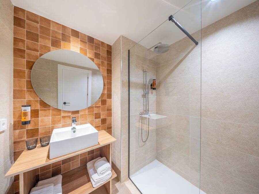 Un baño moderno con un lavabo blanco, un espejo redondo y una cabina de ducha con mampara de vidrio.