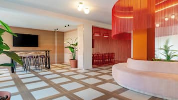 Ein modernes Interieur mit Schachbrettmuster-Boden, einer Sitzecke mit Sofa und Sesseln, einem an der Wand montierten Flachbildfernseher und einer Topfpflanze.