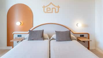Una cama doble con dos mesitas de noche, cada una con una lámpara. La cama tiene un cabecero con el logotipo 'ten'.