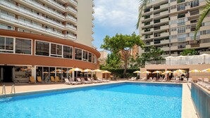 Una piscina con tumbonas y sombrillas, rodeada de edificios altos.
