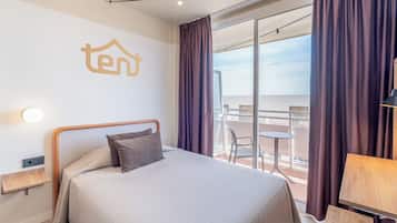 Habitación de hotel con cama, una mesita, una silla, balcón con vistas y un logotipo 'ten' en la pared.