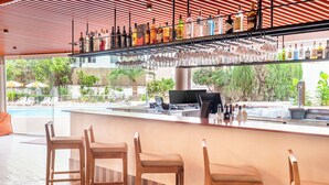 Una zona de bar con una barra alargada, varios taburetes y una amplia variedad de botellas y vasos.