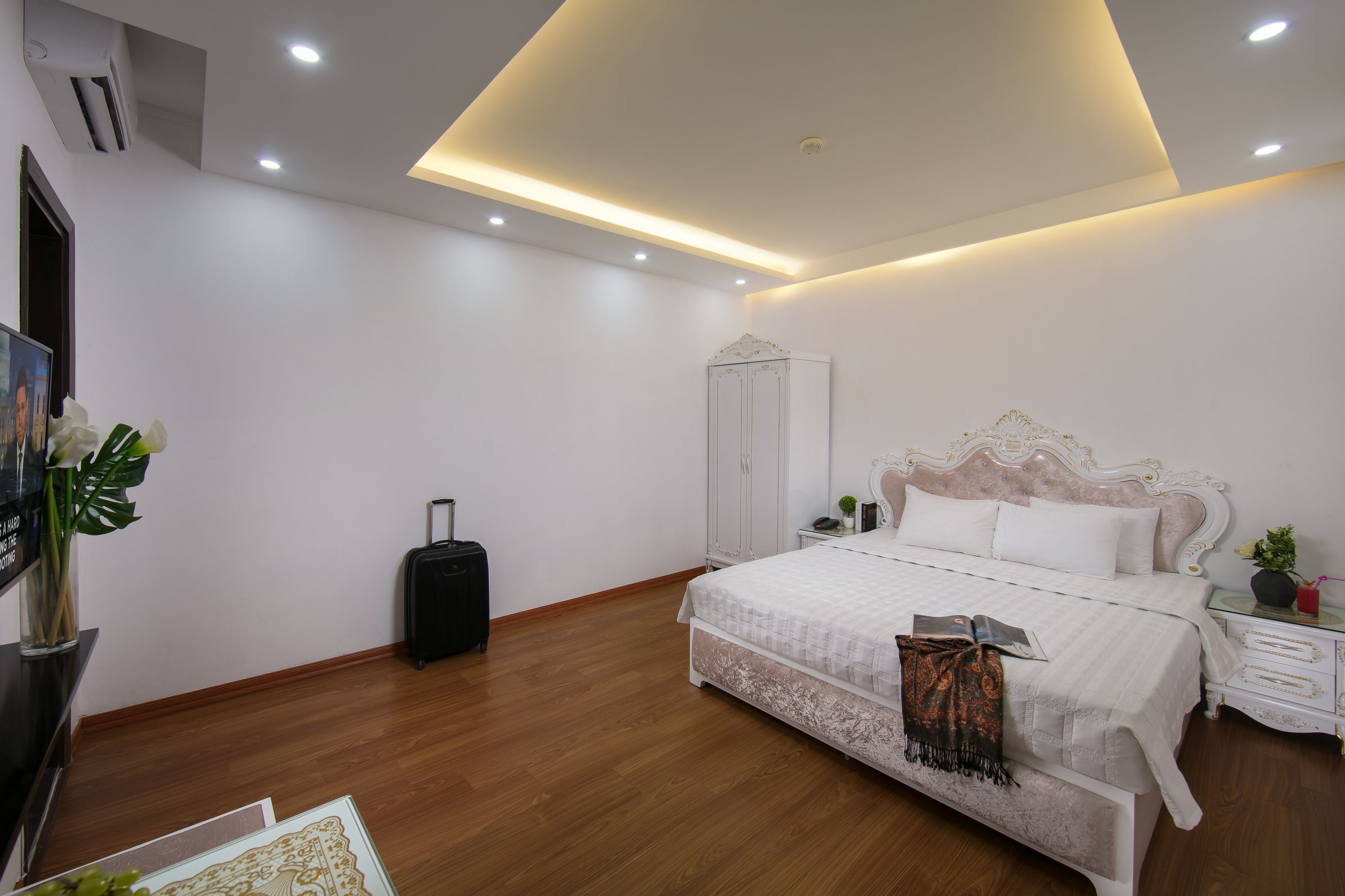 A modern bedroom with a large bed, a bedside table, a wardrobe, and a suitcase.