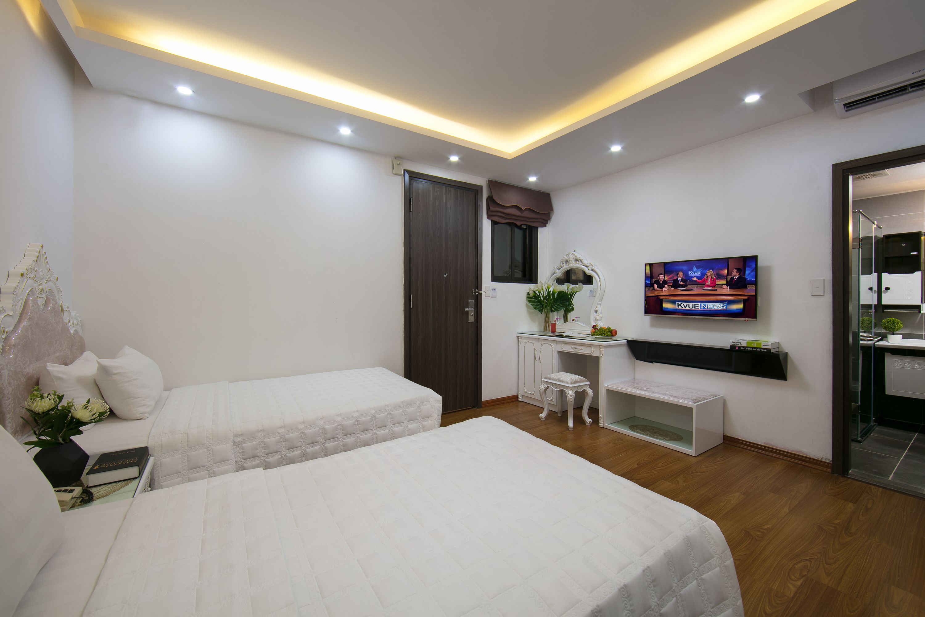 A modern bedroom with two beds, a desk, a TV, and a small seating area.
