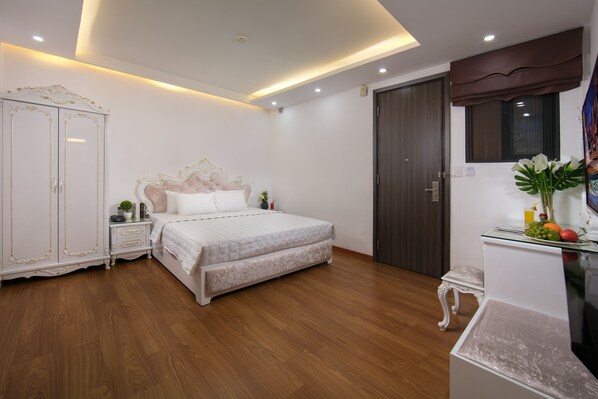 A bedroom with a bed, wardrobe, bedside table, and a small stool. - Kingly Hotel (Hanoi)