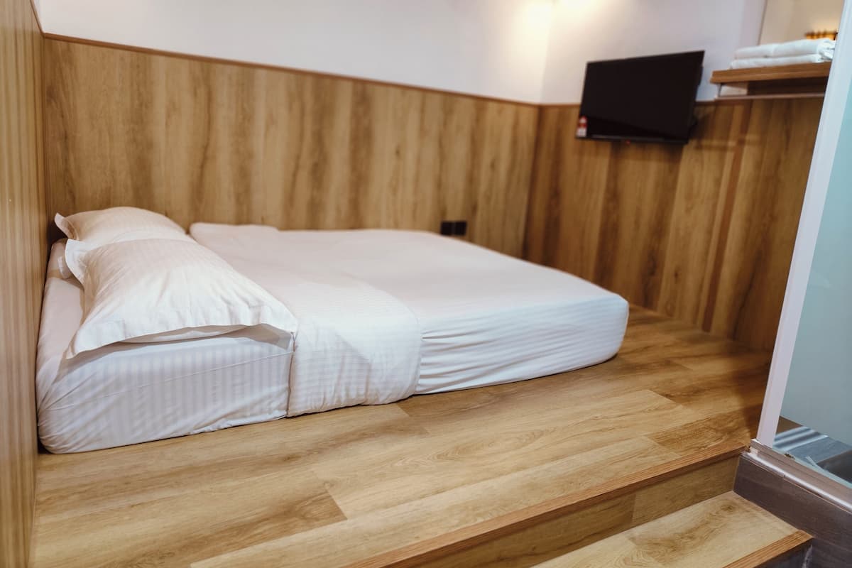 A bed with white linens in a room with wooden paneling and a mounted television.