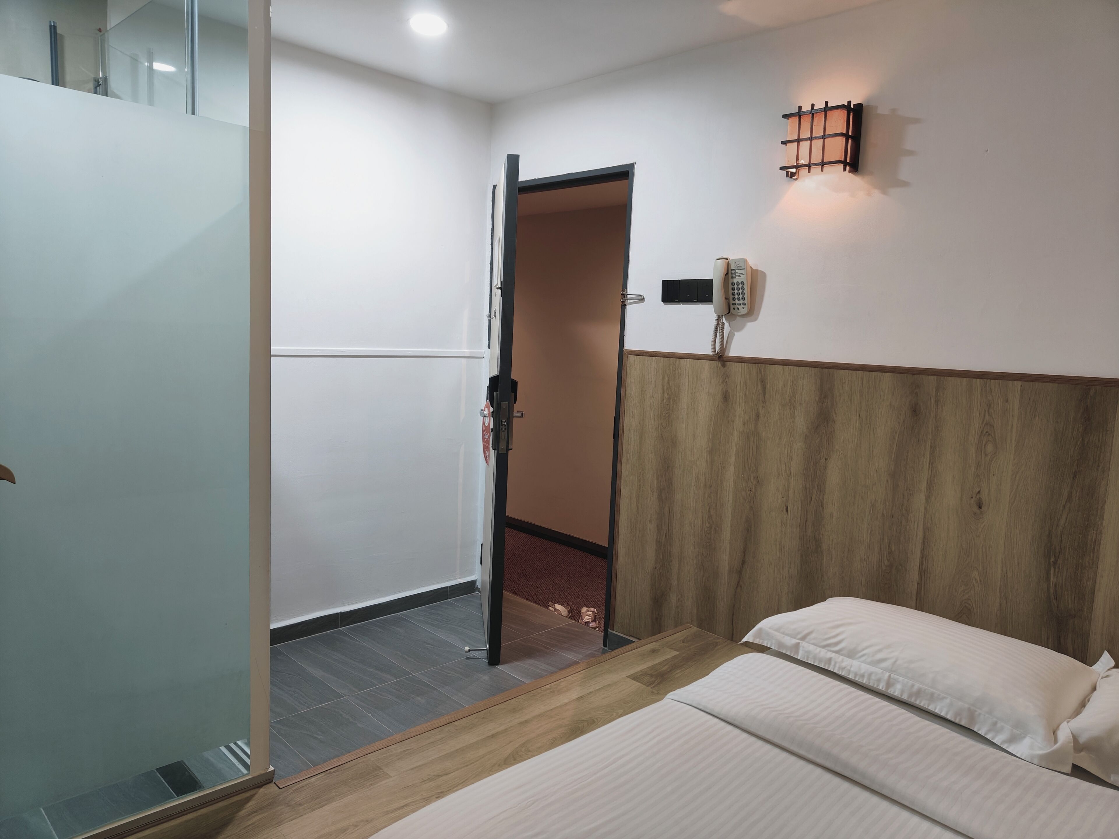 A hotel room with a bed, a wooden headboard, a telephone, and a door leading to another room.