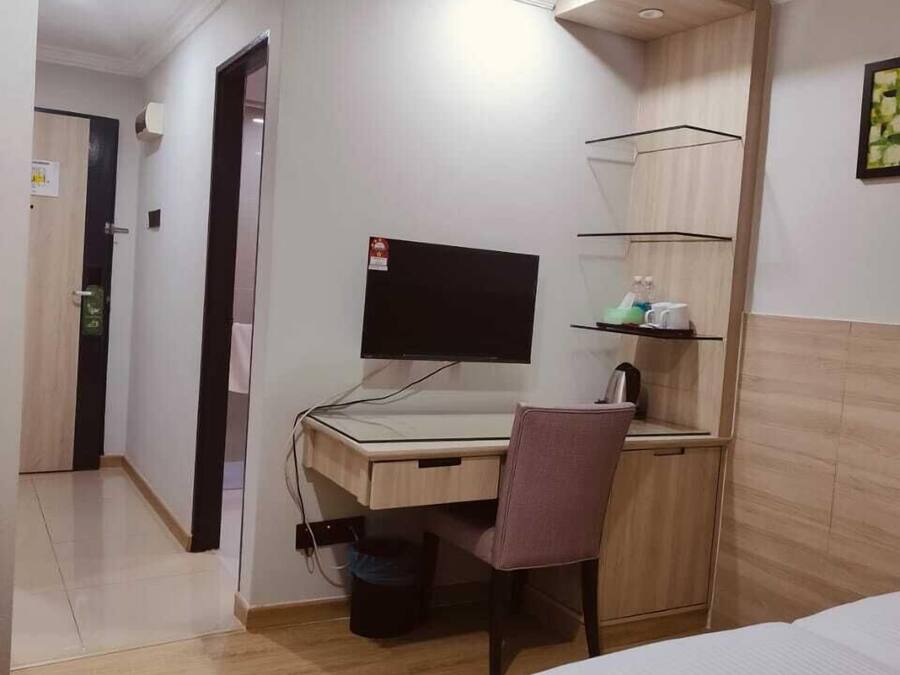 Una camera d'albergo con un letto, una scrivania con un computer, una sedia, un cestino e uno scaffale con articoli da toilette.