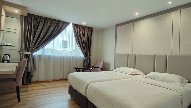 Een hotelkamer met twee bedden, een bureau, een stoel en een groot raam met gordijnen.