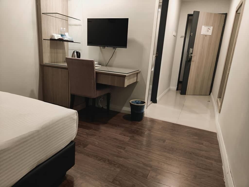 A bedroom with a bed, a desk with a computer, a television, and a small trash bin.