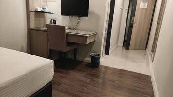 A bedroom with a bed, a desk with a computer, a television, and a small trash bin.