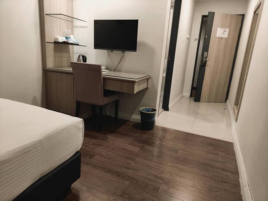 A bedroom with a bed, a desk with a computer, a television, and a small trash bin.