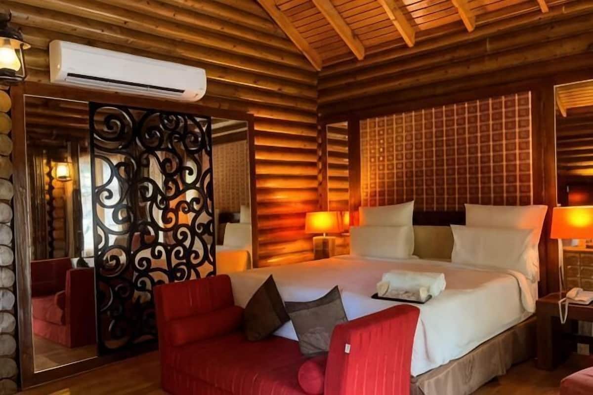 Un dormitorio de estilo cabaña de troncos con una cama grande, un sofá rojo y un panel decorativo de metal.