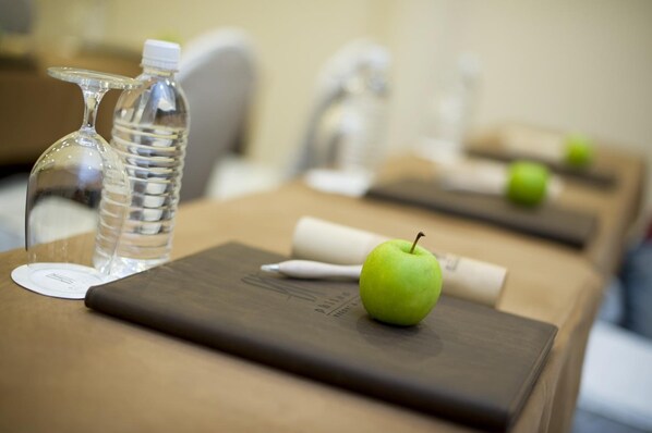 A hotel room with a neatly arranged table featuring a water bottle, a glass, a pen, a notebook, and a green apple.