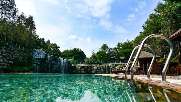 A clear pool with a waterfall backdrop, lounge chairs, and a wooden deck. - Philea Resort & Spa (Malacca City)
