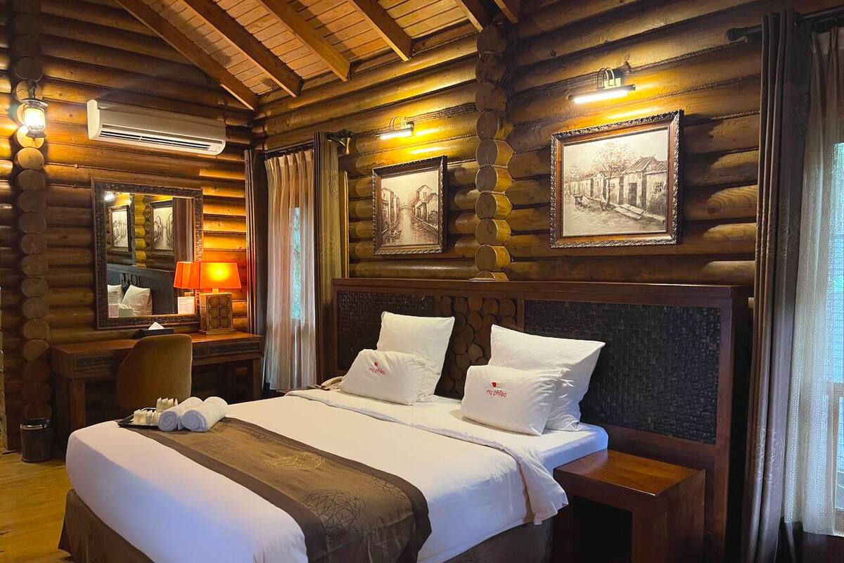 Una habitación tipo cabaña de madera con una cama grande, cabecera de madera y un escritorio con lámpara.