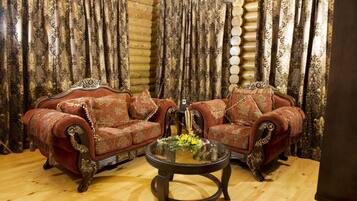 A log cabin interior with two ornate red armchairs facing each other, a glass coffee table with flowers, and patterned curtains.