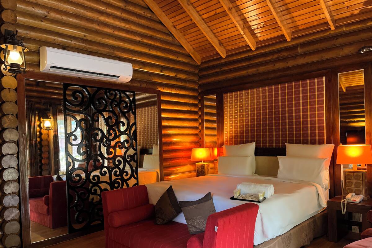 Un dormitorio de estilo cabaña con una cama grande, un sofá tapizado rojo y un espejo con detalles de hierro forjado.
