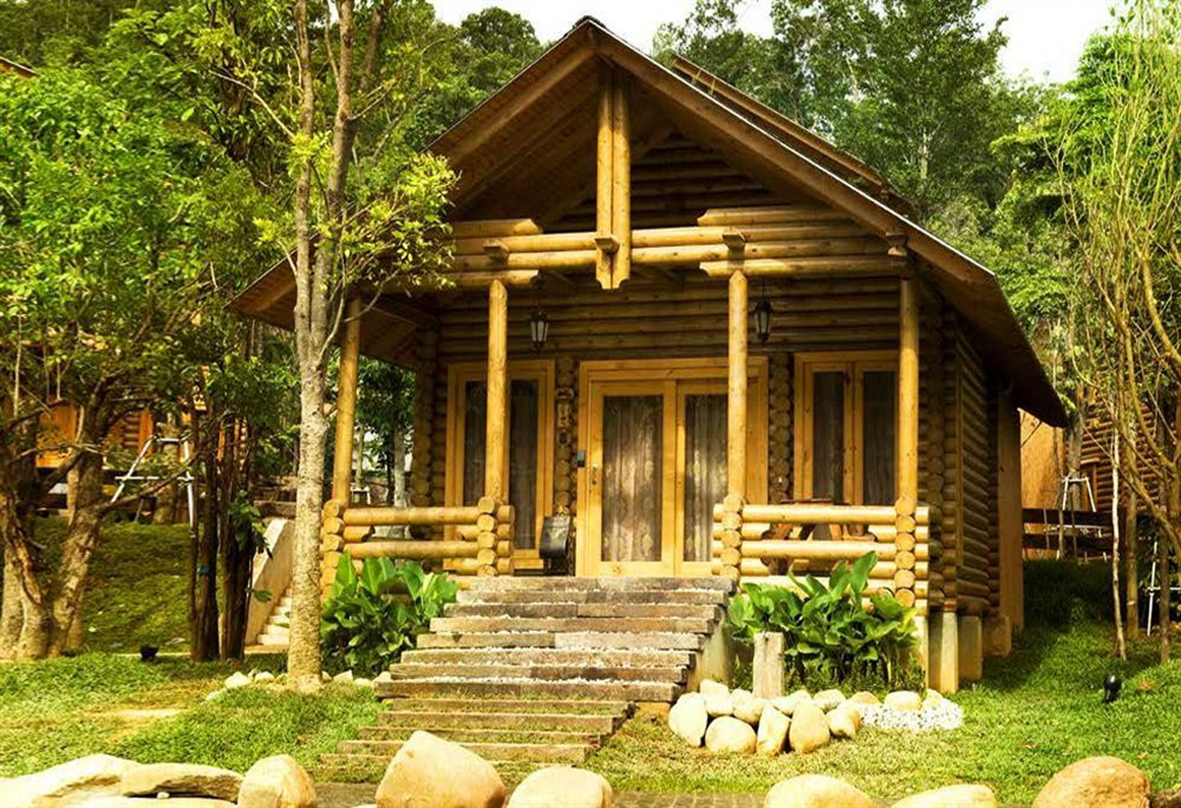 Eine rustikale Holzhütte mit Veranda, umgeben von Grünpflanzen und Steinen.
