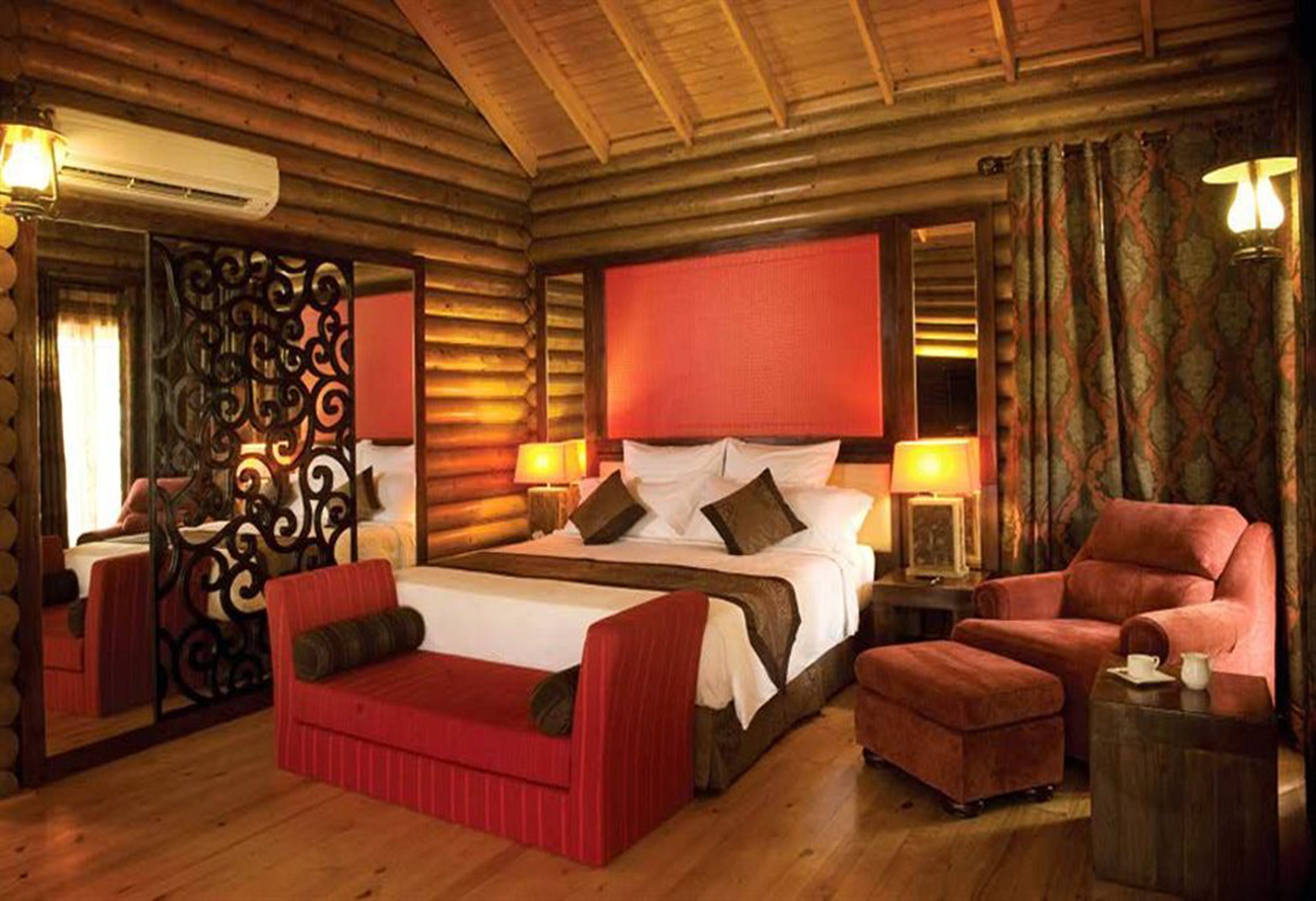 A log cabin-style room with a large bed, two bedside tables, a red sofa, and a red armchair.