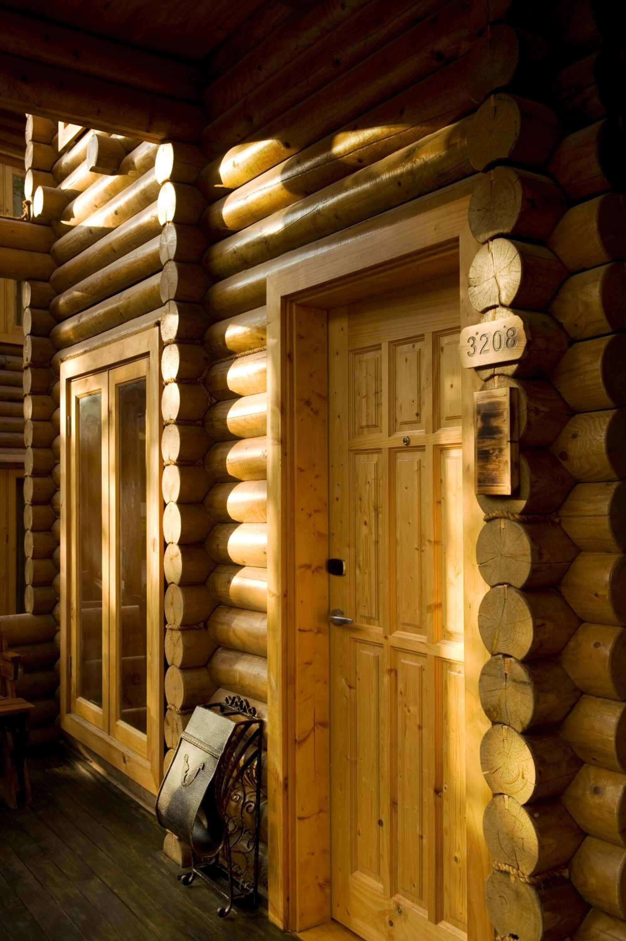 A log cabin interior with a wooden door marked "3208", a bench, and a coat rack.