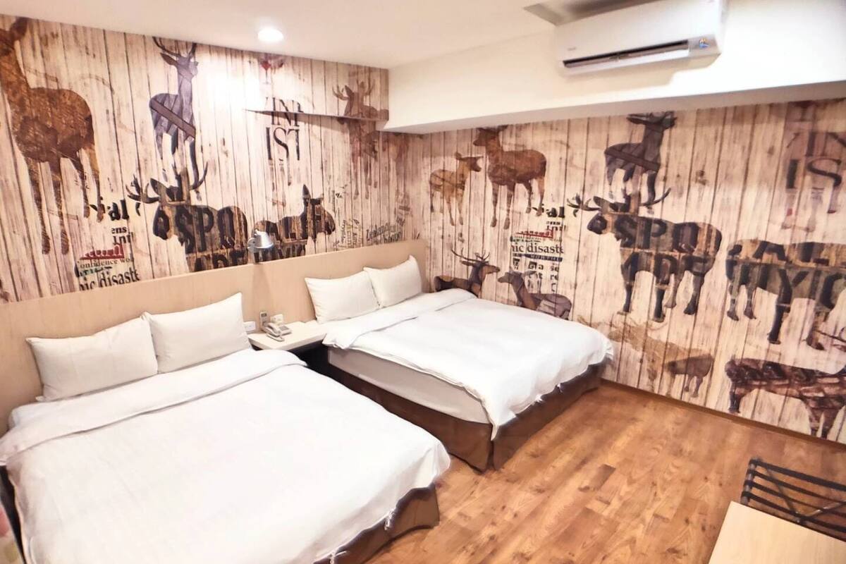 A hotel room with two beds, wooden flooring, and a wall mural featuring deer and elk.